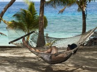 Man relaxing in a hammock strung between palm trees overlooking the ocean at a tropical island resort